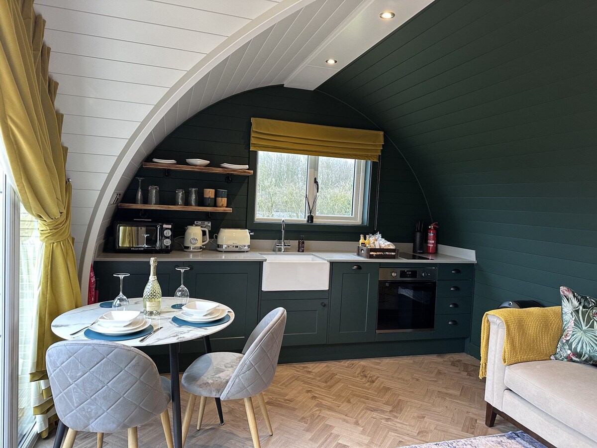 A modern kitchen space is provided, featuring a farmhouse sink, integrated appliances, and open shelving with kitchenware. A round dining table with upholstered chairs sits near a large window adorned with yellow curtains, allowing natural light to fill the area.