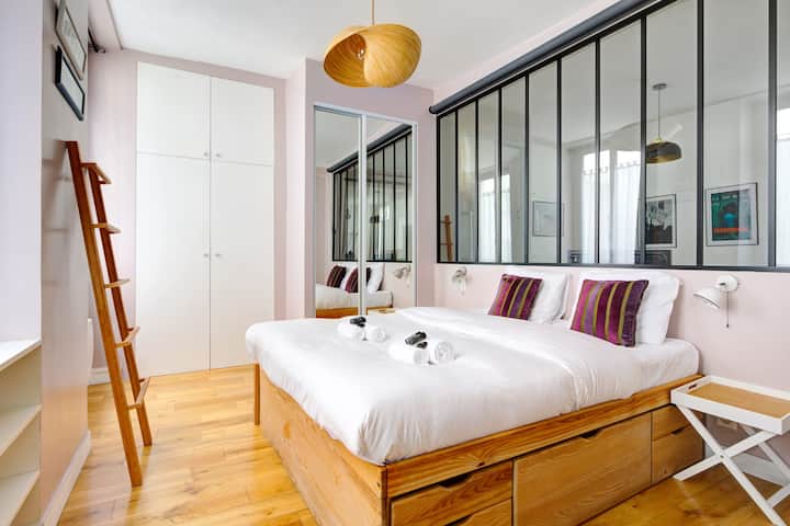 ห้องพักสไตล์โมเดิร์นสดใสพร้อมเตียงคู่หมอนสีสันสดใสและพื้นไม้สีอ่อน ที่เก็บของบิวท์อินใต้เตียงตู้เสื้อผ้าสีขาวและกันสาดสีดำที่ให้ความรู้สึกแบบอุตสาหกรรมที่สง่างาม ตกแต่งอย่างพิถีพิถันสะดวกสบายและอบอุ่น