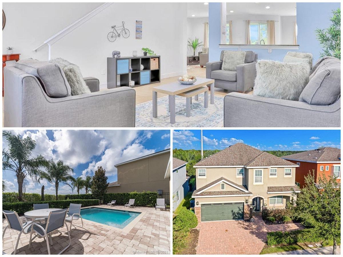 A bright and inviting living area showcases modern furniture with soft cushions, complemented by a decorative wall piece. In another section, a spacious backyard features a private pool surrounded by lounge chairs and lush greenery, under a clear blue sky.