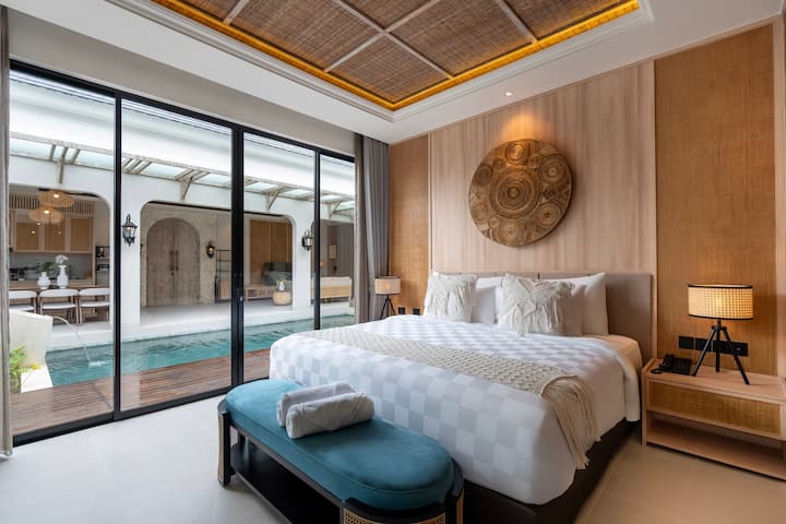 Dhomë gjumi me krevat dopio "king", tone neutrale dhe dekor muri prej palme kacavjerrëse.