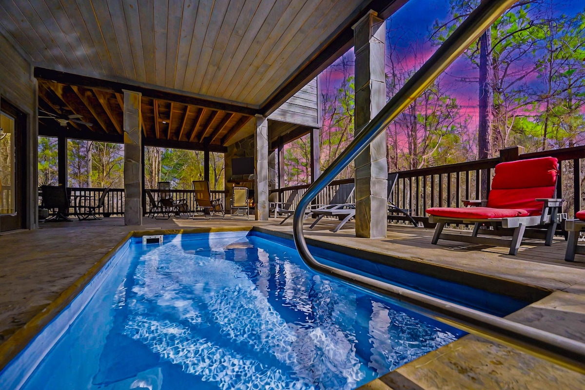 The image captures a private pool nestled under a wooden deck, flanked by natural wood pillars. A gentle gradient of colors fills the sky, adding a serene ambiance. A lounge chair is positioned nearby, offering a relaxed spot for enjoying the tranquil outdoor setting.