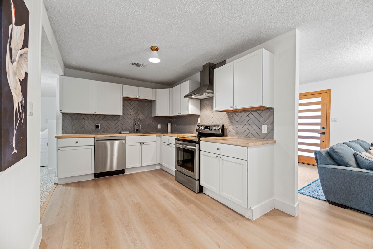 The updated kitchen features stainless steel appliances, including a sleek stove and refrigerator. Granite countertops complement the custom cabinetry, while a herringbone backsplash adds texture. Ample natural light brightens the space, showcasing modern design elements and a functional layout.
