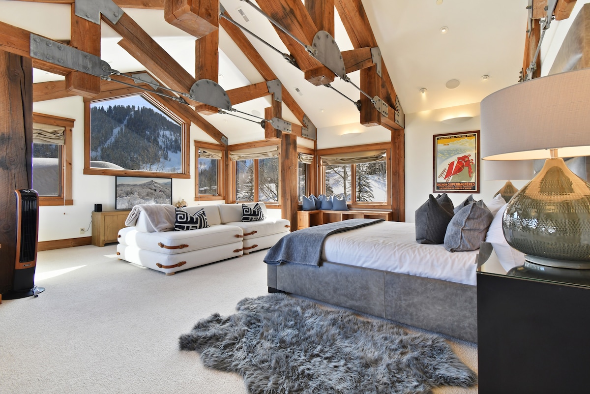 Stora fönster sitter framför sängen i det primära sovrummet, med en stor soffa framför ett underhållningscenter och TV.