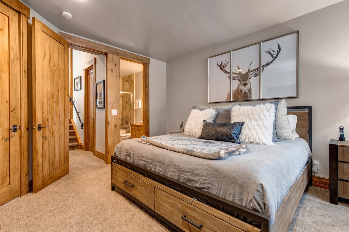 A bedroom with a bed, a night stand, and a bathroom.