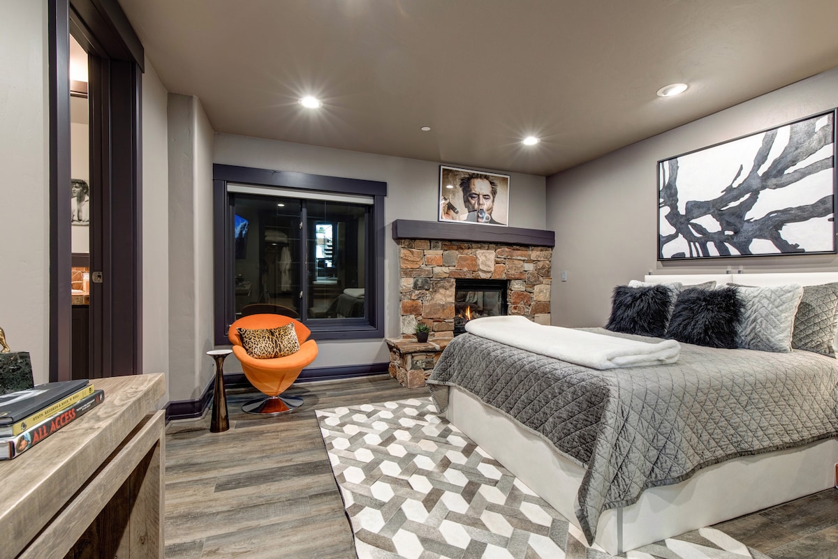 A bedroom with a bed, a small fireplace, and a chair.