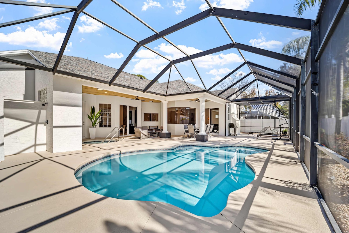 An outdoor space is enclosed with a screened patio, featuring a clear blue heated pool surrounded by lounge chairs. The home is visible in the background, showcasing large windows that provide natural light to the interior.