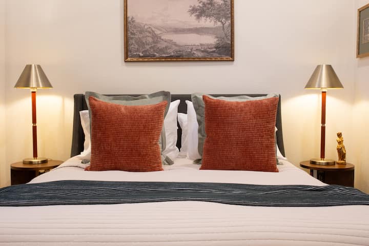 Lijepo uređen krevet s toplim tonovima i blagim osvjetljenjem.