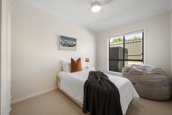 Ნათელი და მიმზიდველი საძინებელი ერთადგილიანი საწოლით, თბილი ტონიანი აქცენტებით და დიდი ლობიოს ჩანთით დამატებითი კომფორტისთვის.