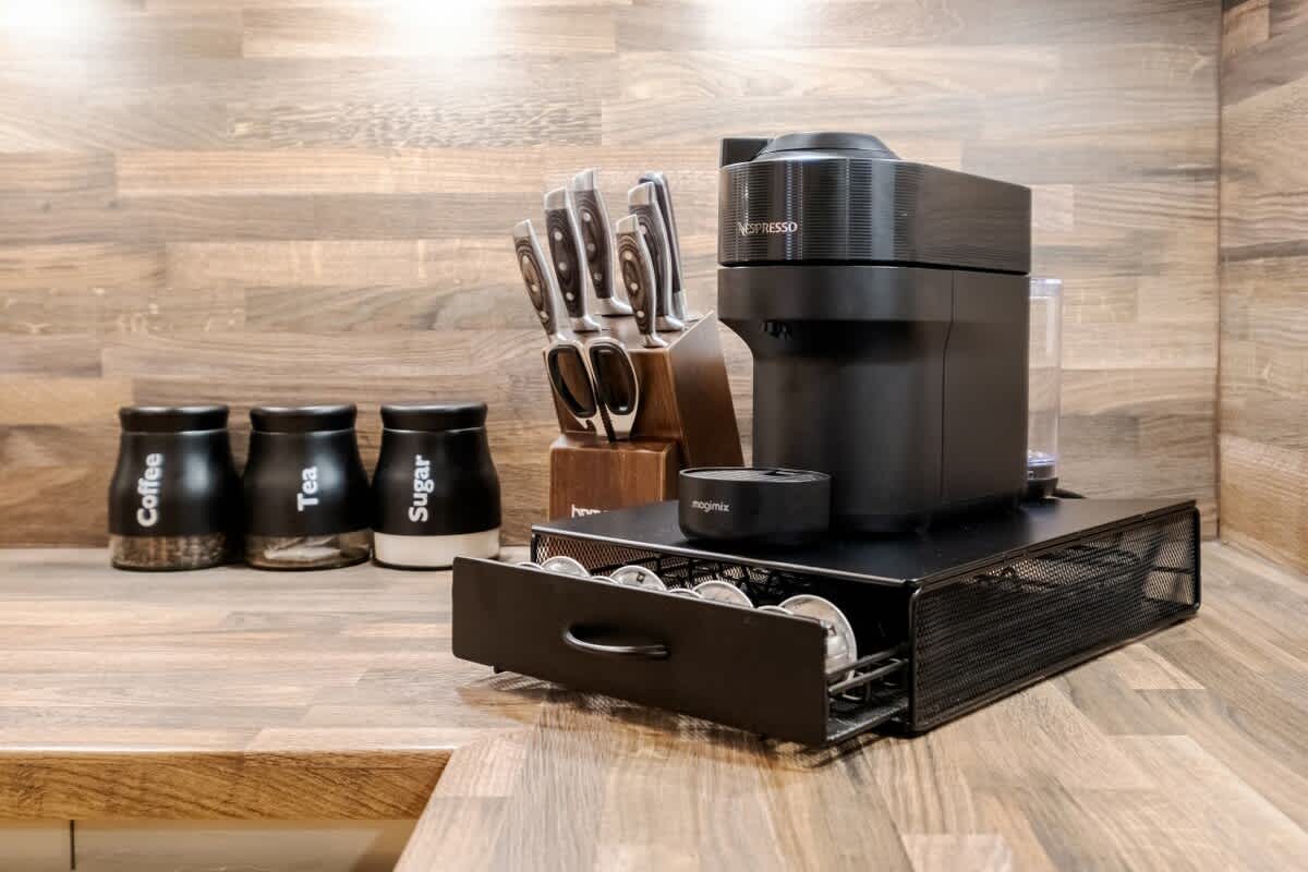 A modern kitchen countertop showcases a sleek Nespresso machine next to a set of kitchen knives within a wooden block. Nearby, canisters labeled 'Coffee,' 'Tea,' and 'Sugar' provide convenient storage, enhancing the fully equipped space.
