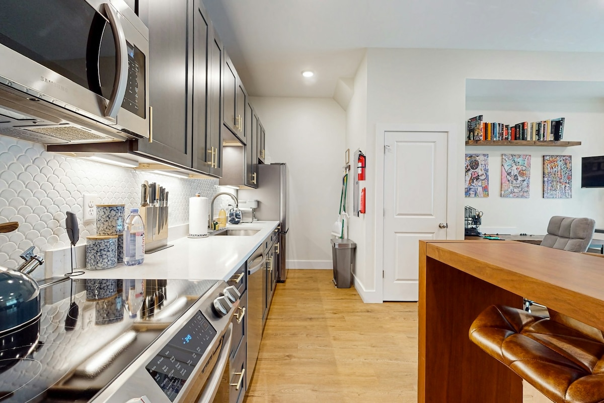 A modern kitchen is equipped with stainless steel appliances, including a microwave and oven. Quartz countertops offer ample space, while decorative tile backsplashes add texture. A wooden bar with high seating overlooks the kitchen area, enhancing functionality and style.