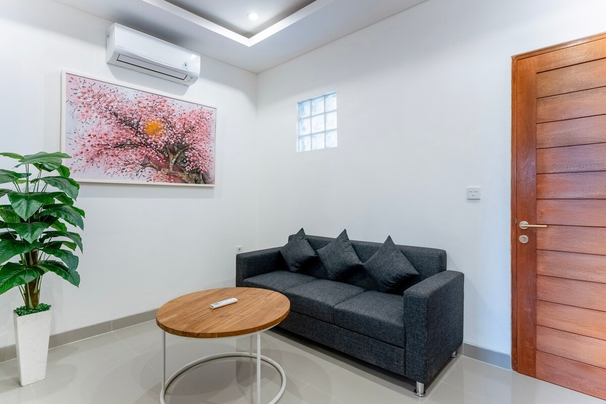 Уютна всекидневна със стилен диван, телевизор с плосък екран и произведения на изкуството на стената. Перфектно място за отдих или за филмова вечер на закрито.