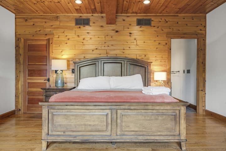 Lujoso dormitorio principal con cama tamaño king, baño privado y paredes con paneles de madera.