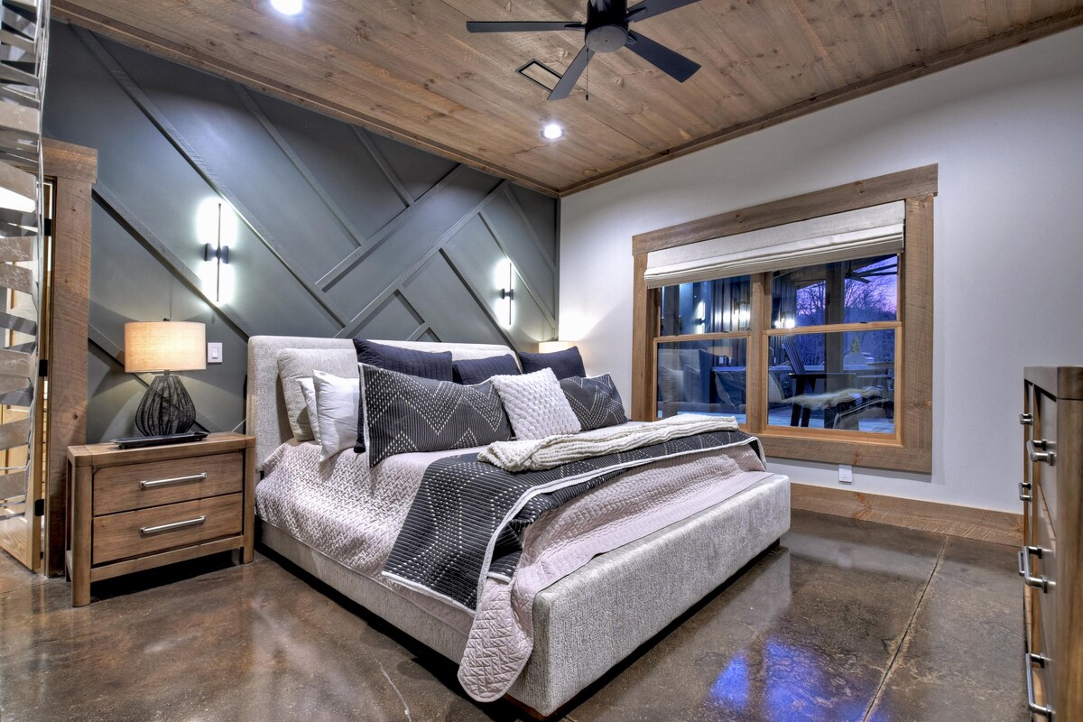 Модерна спалня с плюшено голямо двойно легло, елегантно осветление и изискани дървени акценти.