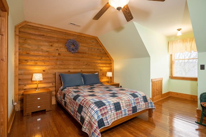 ห้องนอนที่มีเสน่ห์พร้อมแผงไม้แบบชนบทผ้าห่มที่อบอุ่นและเพดานลาดชันที่สร้างสถานที่พักผ่อนที่เป็นกันเองและผ่อนคลาย