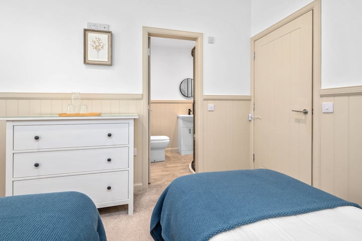 Светла и уютна стая с 2 отделни легла с меки сини акценти, елегантен бял скрин и самостоятелна душ кабина за допълнително удобство.