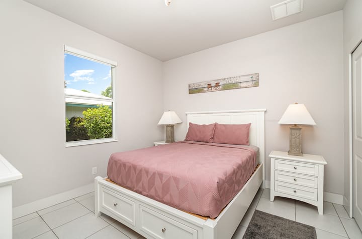 Acogedor dormitorio de invitados con una cómoda cama tamaño queen, muebles blancos brillantes y vistas al jardín.