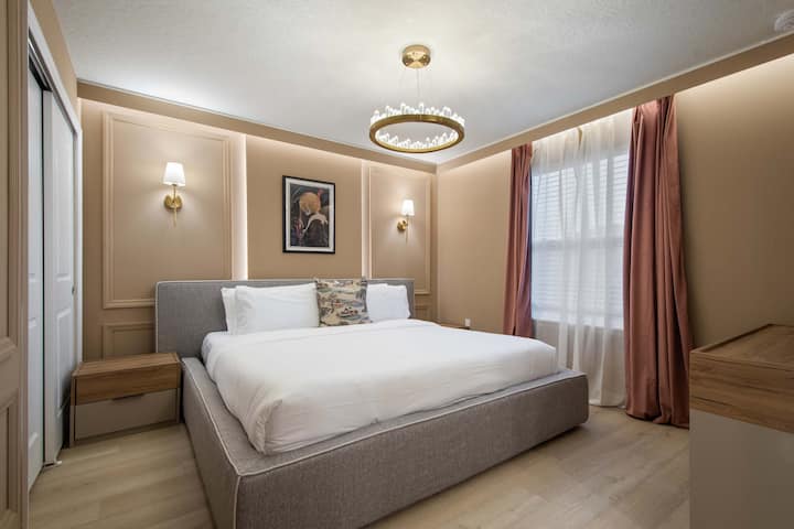 Dormitorio elegante con tonos cálidos, lujosa cama king e iluminación clásica moderna.