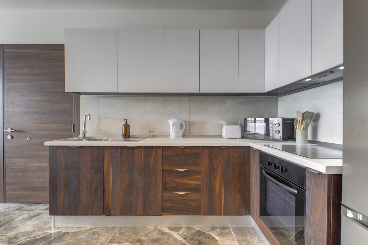 A modern kitchen is equipped with sleek cabinetry in warm wood tones and light-coloured upper cabinets. Counter space is available for meal preparation, with appliances including a kettle, toaster, and coffee maker neatly arranged. A stylish sink and modern oven complete the functional setup.