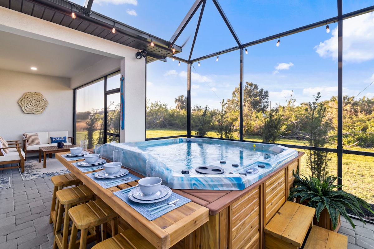 A private hot/cold spa is featured within a screened area, accompanied by a wooden dining table set for six with neatly arranged tableware. Natural light floods the space, highlighting the lush greenery visible through the large glass walls.