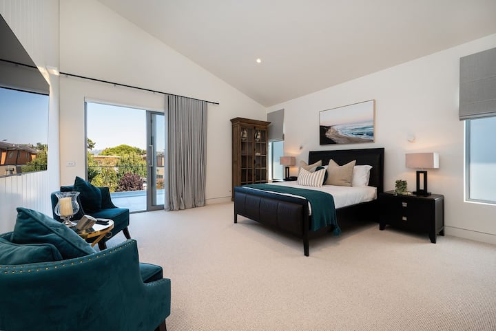 Enorme hoofdslaapkamer met flatscreen-tv, fauteuils en uitlopend op het balkon.