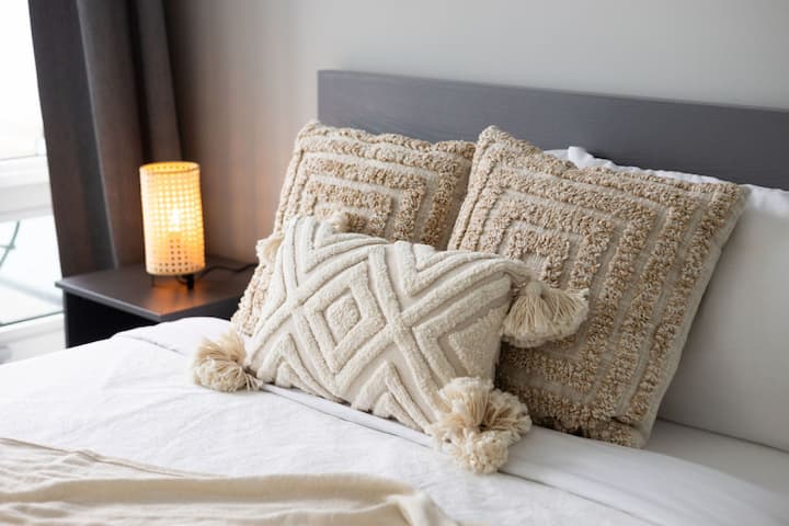 Admira las almohadas texturizadas y el cálido resplandor junto a la cama, perfecto para relajarse después de un día ajetreado