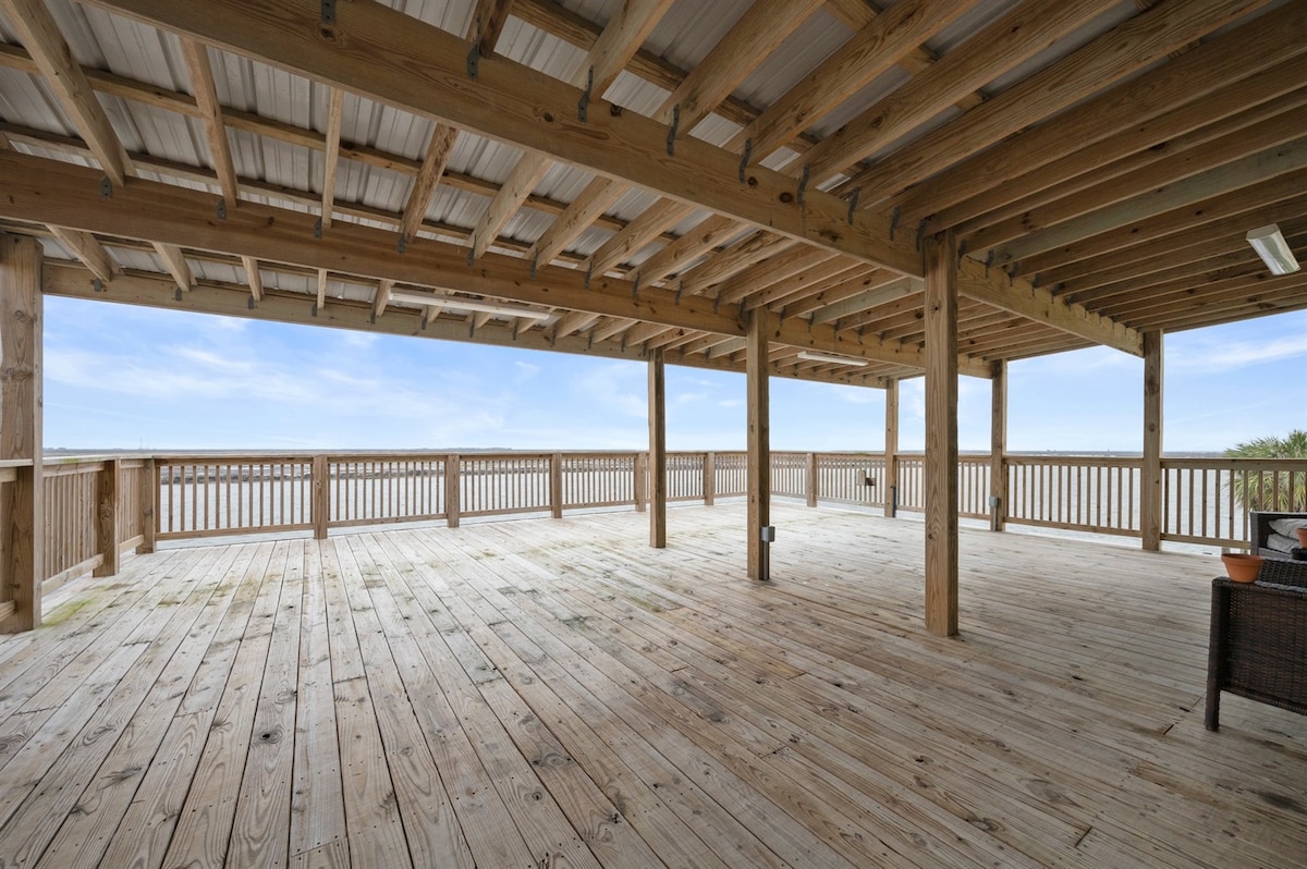 A spacious outdoor deck is featured, with wooden beams supporting the roof. The area is elegantly framed by railing, offering an unobstructed view of the surroundings. The wooden floor adds a rustic charm, inviting relaxation and gatherings.