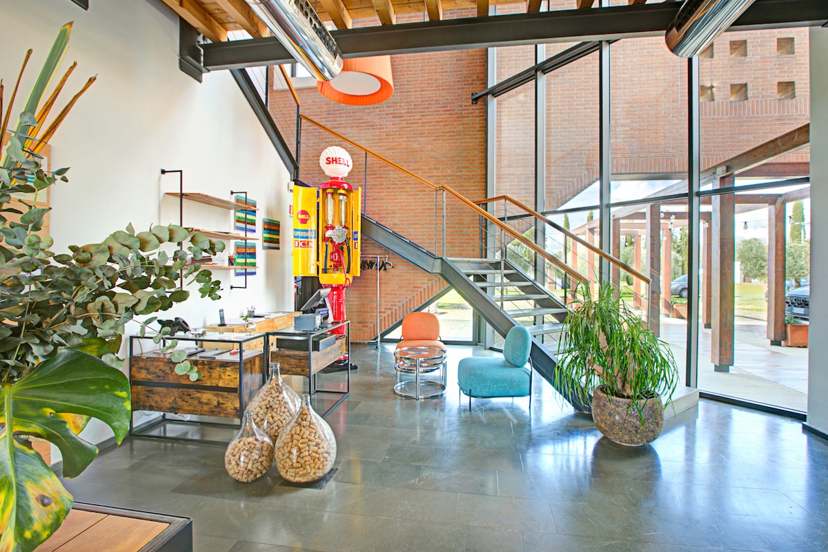 A spacious entrance area features high ceilings and large glass windows, allowing natural light to fill the space. A unique vintage vending machine and colorful seating enhance the inviting atmosphere. Potted plants and decorative elements provide a touch of greenery, creating a modern and welcoming ambiance.
