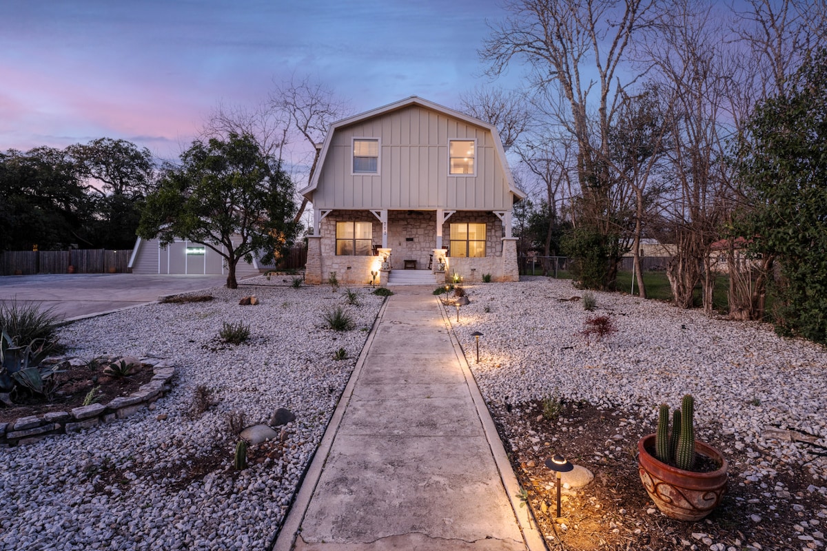 The entrance of the property is framed by a gravel pathway leading to a two-story structure. Soft outdoor lighting highlights the walkway, while landscaped areas with various plants and stones create a serene atmosphere.