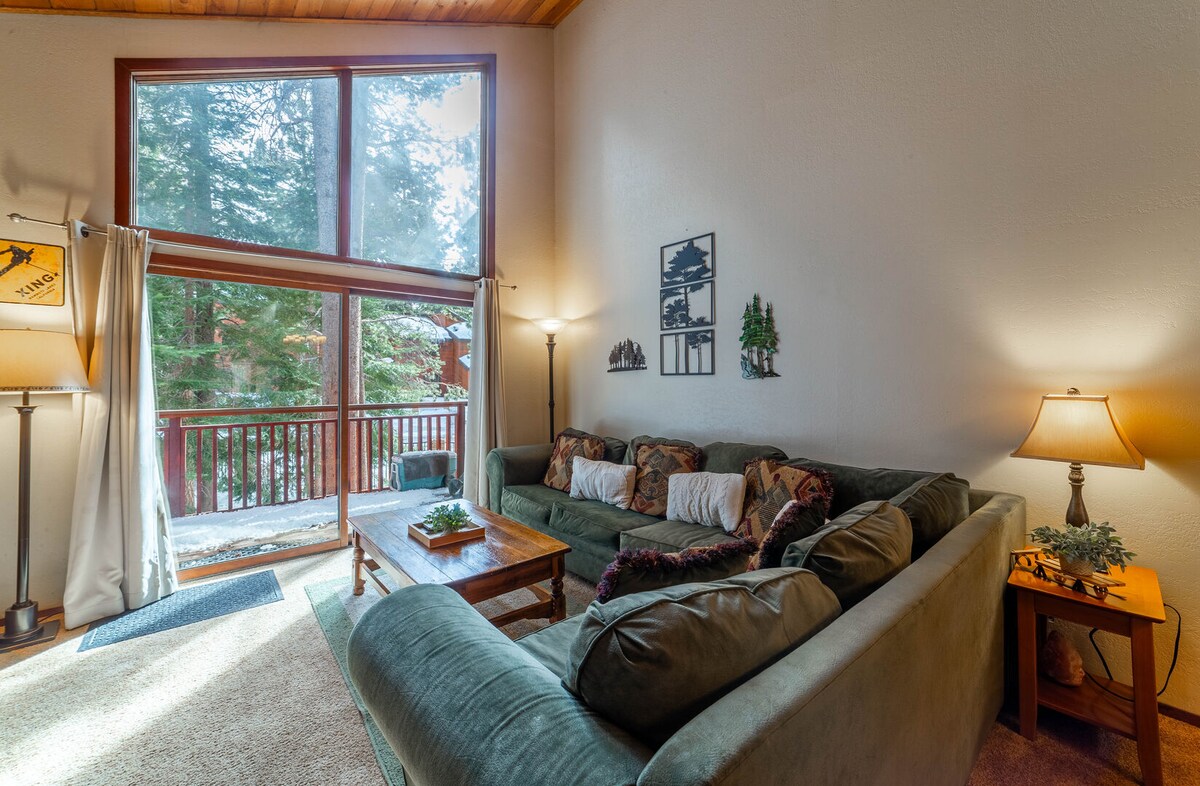 ห้องนั่งเล่นพร้อมโซฟาตัดขวางขนาดใหญ่มองเห็นต้นสนอันงดงาม