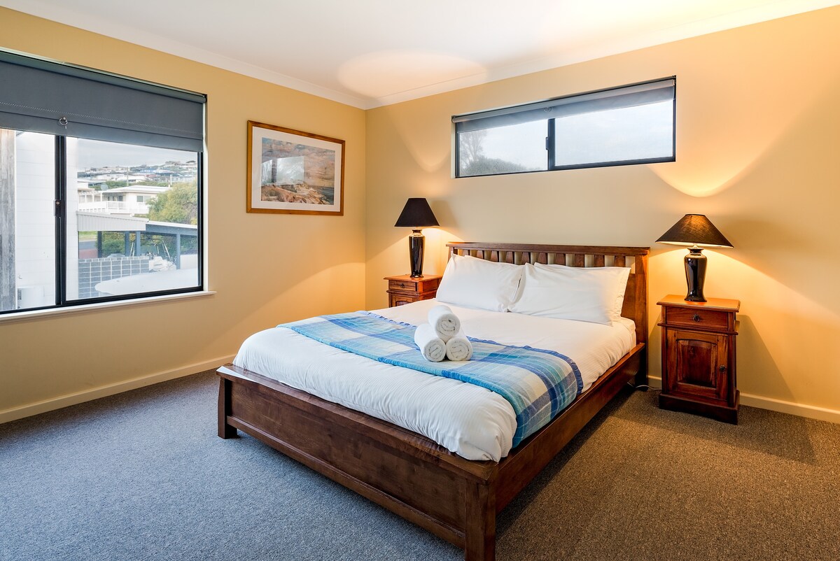 ห้องนอนควีนไซส์หลักชั้นบนประกอบด้วยเตียงนอนสบายๆโต๊ะข้างเตียงและแสงธรรมชาติอ่อนๆ