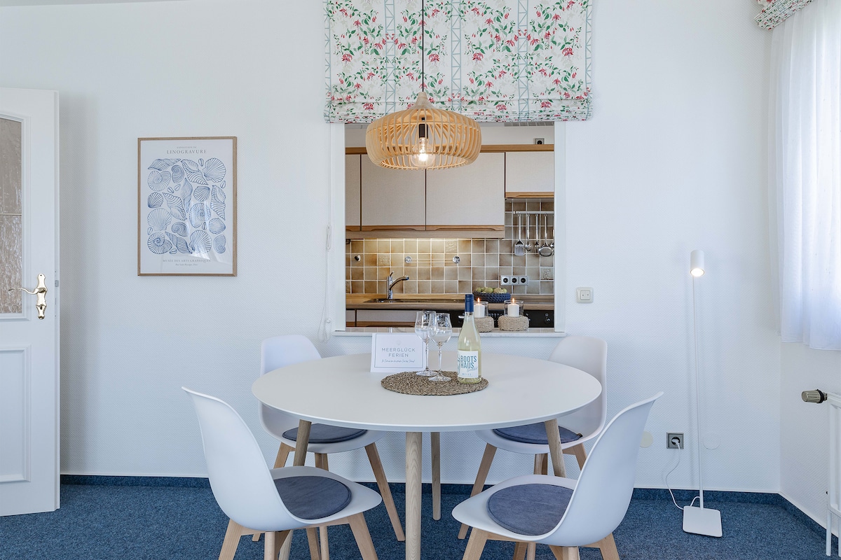A bright dining area is presented with a circular white table surrounded by four light-colored chairs. Above, a woven pendant light adds a touch of warmth. A small decorative arrangement sits on the table, with a modern lamp in the corner enhancing the inviting space.