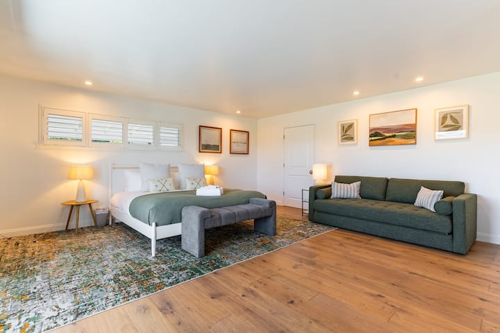 Kamar tidur utama yang luas dengan tempat tidur king, sofa, TV, dan akses balkon.