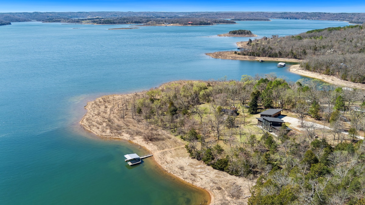 Aerial view of Beaver Lake showcases its expansive waters and gentle curves of the shoreline. Lush greenery surrounds the edges, and the image captures a boat docked at the water's edge, emphasizing the accessibility and natural beauty of the area.