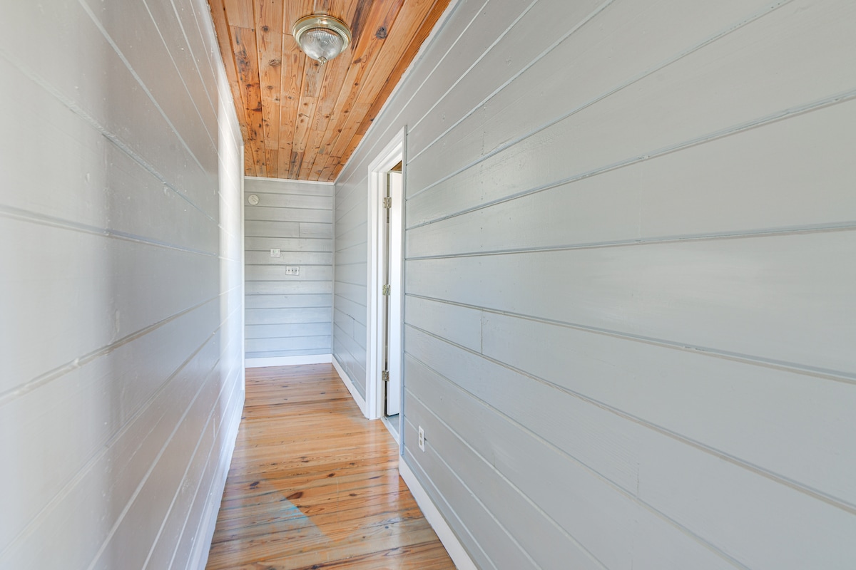 A narrow hallway is displayed with light-colored wooden walls and a natural wood ceiling. Warm tones of the hardwood floor complement the overall aesthetic. The hallway leads to doorways on the right, providing access to various rooms within the duplex unit.