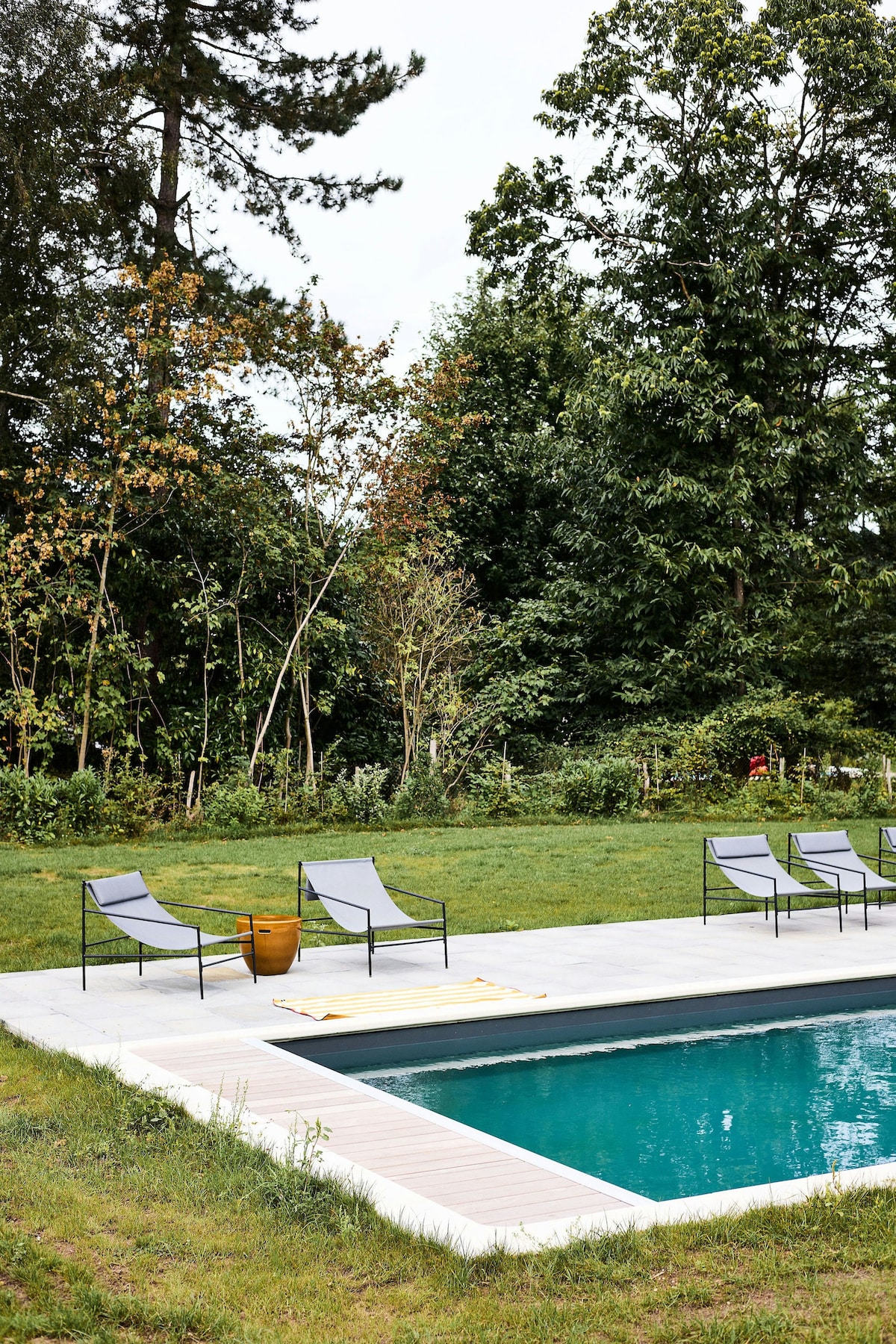 The outdoor area features a heated swimming pool surrounded by a spacious deck. Four lounge chairs are positioned nearby, offering a place to relax. Lush greenery and trees frame the area, creating a serene and inviting environment.