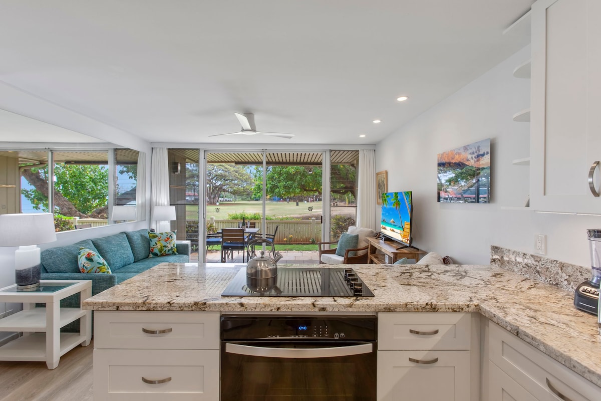 An open-concept living space features a modern kitchen with a large granite island and contemporary appliances. A comfortable seating area includes a turquoise couch adorned with colorful pillows. Large sliding glass doors provide views of the outdoor space, enhancing natural light throughout the room.