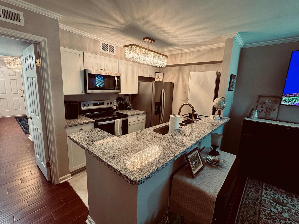 The kitchen features a modern design with granite countertops and stainless steel appliances. A chandelier provides overhead lighting, while a small decorative globe is placed on the counter. The open layout encourages a seamless flow between living areas.