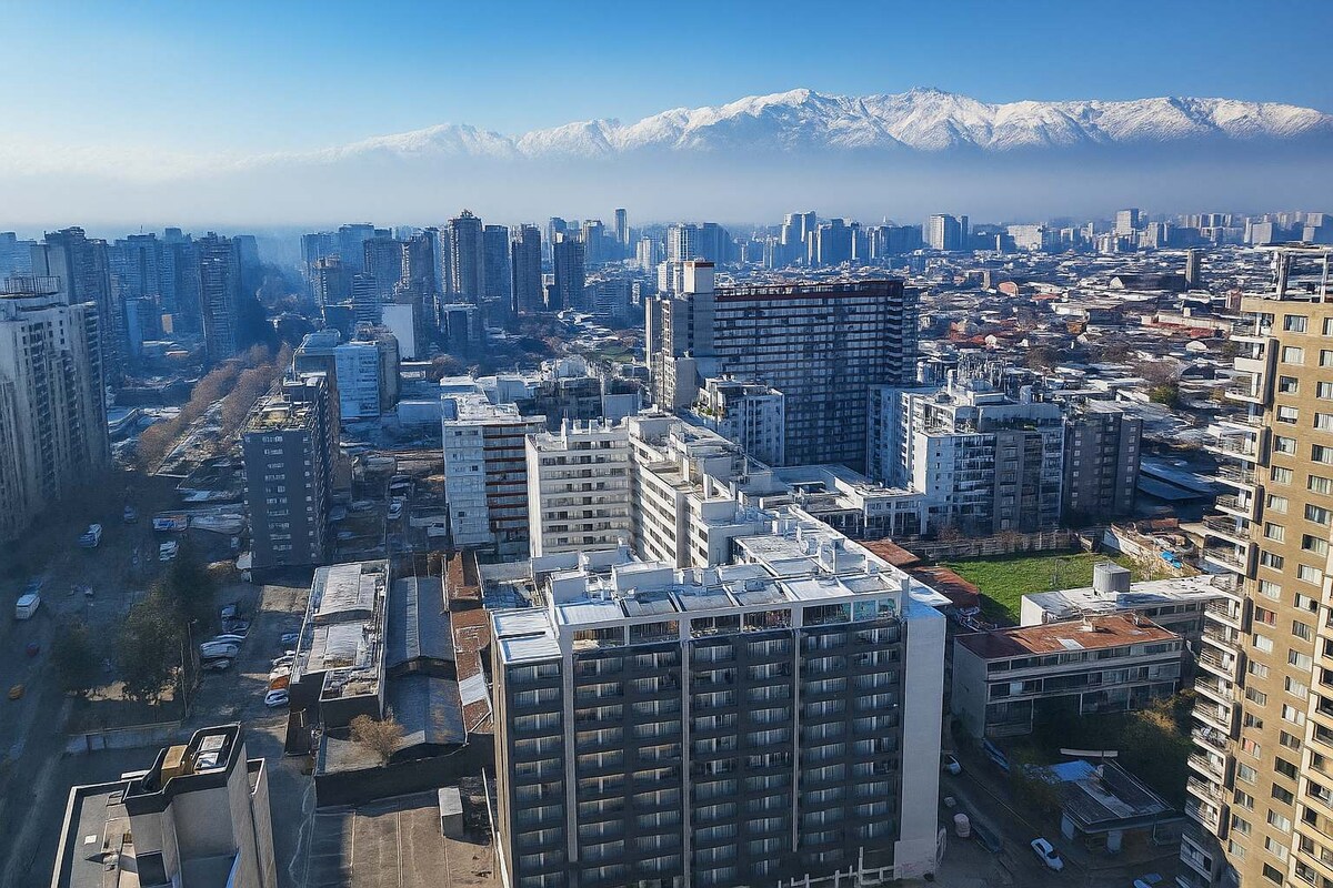 A panoramic view of the city of Santiago is captured from a high vantage point, showcasing both urban structures and scenic mountains in the background. The snow-capped peaks contrast with the cityscape, illustrating the vibrant blend of nature and urban life.