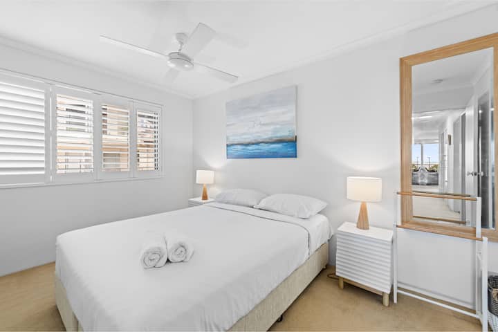 Dormitorio luminoso con obras de arte costeras y lámparas de noche gemelas.