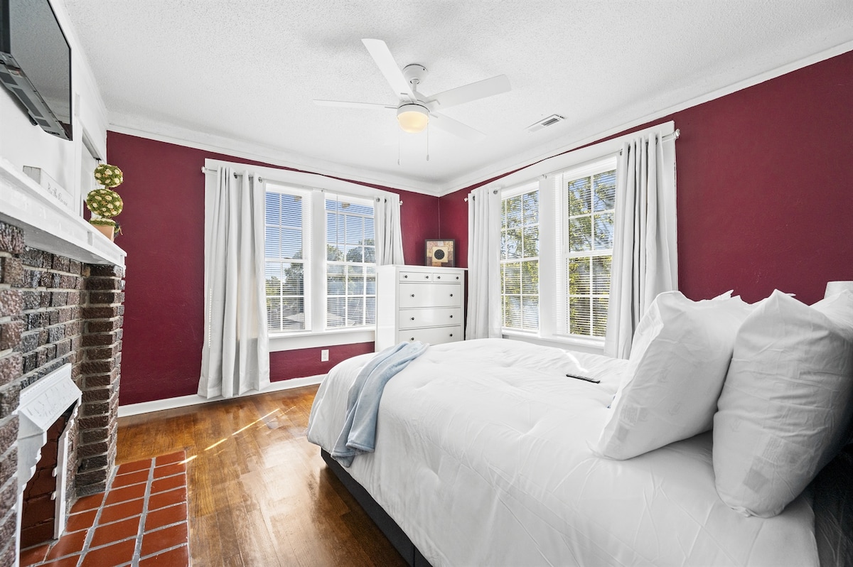 ¡Da la bienvenida a nuestro encantador bungalow! El dormitorio cuenta con ricas paredes rojas y una acogedora cama blanca adornada con almohadas suaves y un tiro azul claro, lo que agrega un toque de elegancia. Una llamativa chimenea de ladrillo sirve como punto focal, complementada con sábanas blancas