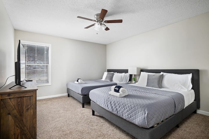 宽敞的卧室，配有两张舒适的标准双人床、一个吊扇和一台智能电视。