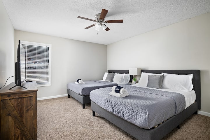 Priestranná spálňa s dvoma manželskými posteľami, stropným ventilátorom a komodou s inteligentným televízorom.