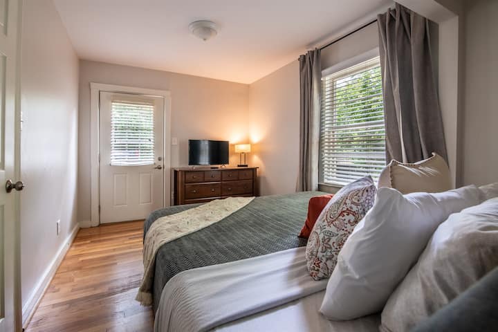 Očarujúca spálňa s manželskou posteľou, komodou, televízorom a oknami, ktoré napĺňajú priestor svetlom.