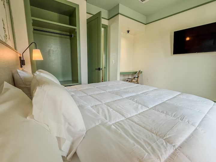 Luminoso dormitorio de invitados con una lujosa cama tamaño king, decoración costera y relajantes tonos neutros.