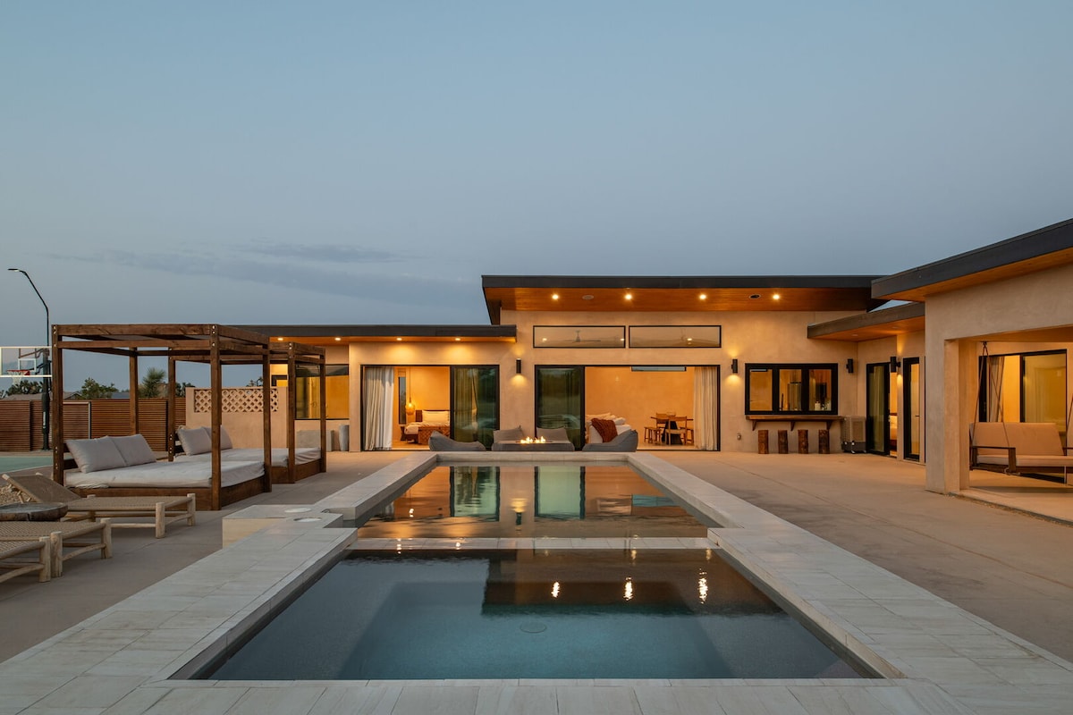 An expansive outdoor space features a tranquil pool, surrounded by seating areas and a pergola. Large glass doors lead into the interior, with soft lighting highlighting the inviting atmosphere as evening sets in.