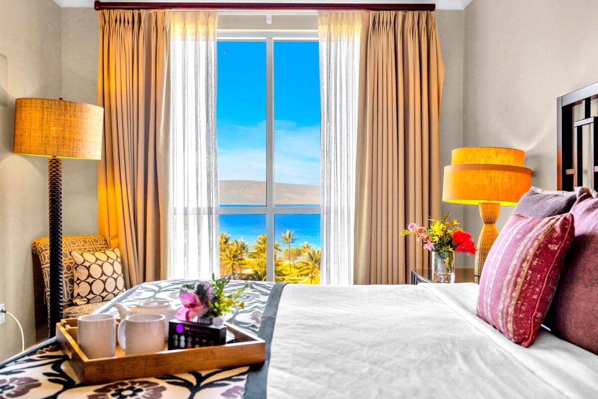 King primary bedroom with bright window views and cozy seating area.