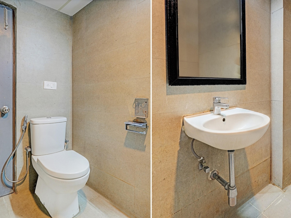 The clean and modern bathroom features a minimalist design with stone walls. On the left, a compact toilet is presented alongside a toilet paper holder. On the right, a wall-mounted sink is equipped with a sleek faucet and (no visible storage space), complemented by a simple square mirror.