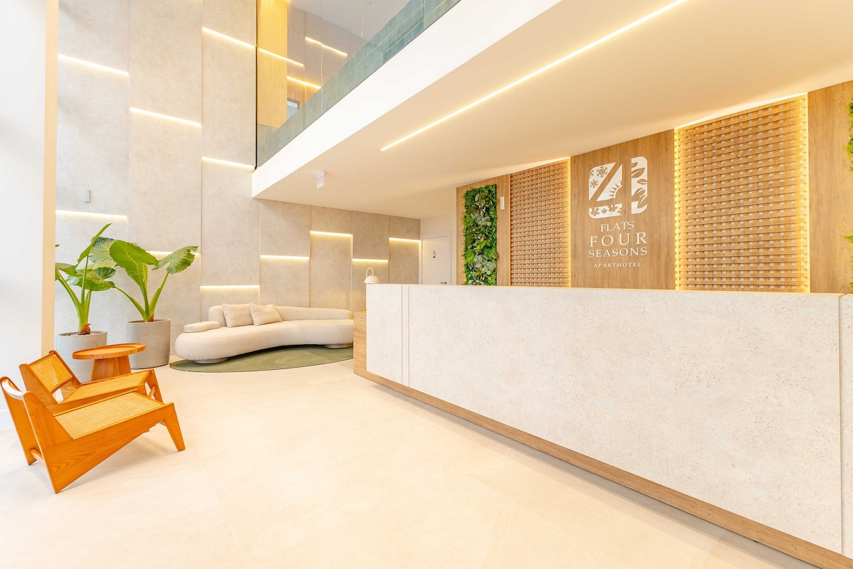 The reception area features a streamlined front desk made from a light-colored material, complemented by greenery and soft lighting. Comfortable seating options include a curved sofa and a wooden chair, creating an open and airy space with a modern aesthetic.