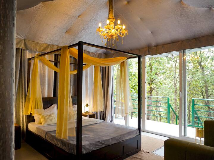 تتميز غرفة النوم الواسعة والهادئة في الخيمة بسرير فخم بأربعة أعمدة وإضاءة ناعمة ونوافذ كبيرة تطل على الغابة. تصميم مدروس، ومقاعد مريحة، تخلق ملاذًا هادئًا مغمورًا بالراحة والطبيعة.