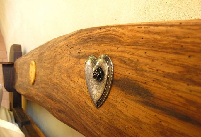 A close-up view of a wooden headboard features an intricately designed heart-shaped decoration. The natural texture of the wood is highlighted, showcasing its rich grain and warm tones.